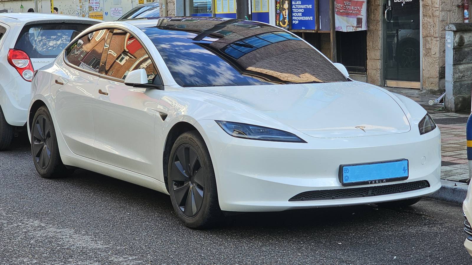 A Pearl White Tesla Model 3 sedan with a black glass roof parked at the kerb on a city street