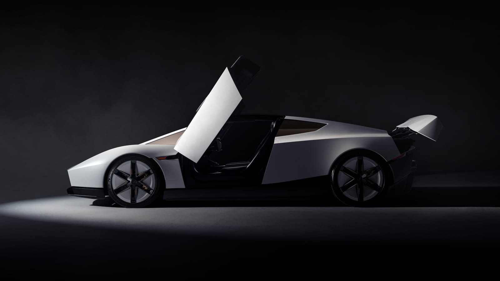A white Tesla Roadster in side profile under a spotlight, with its gullwing door raised and rear wing up