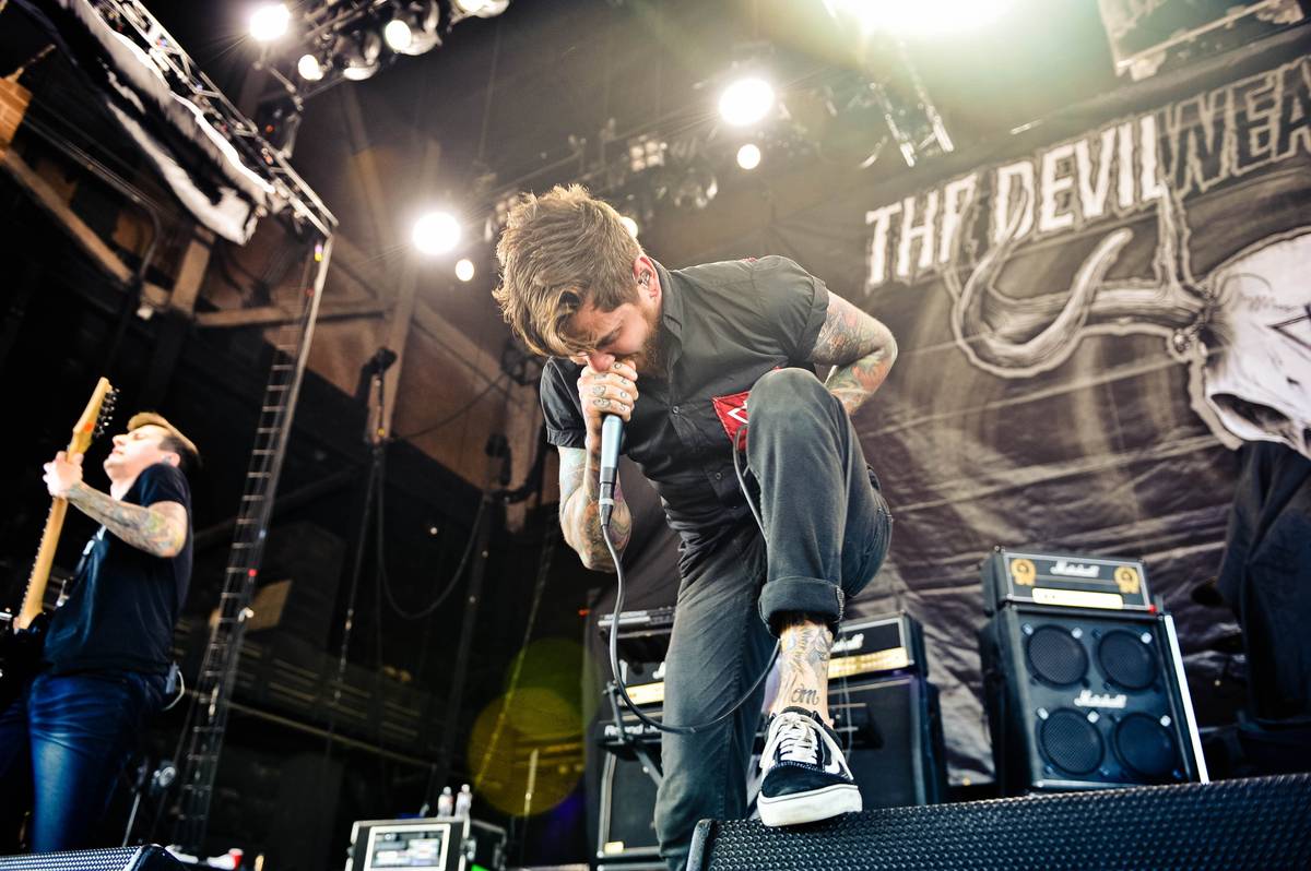 The Devil Wears Prada singer Mike Hranica crouching on a monitor in front of the band's banner