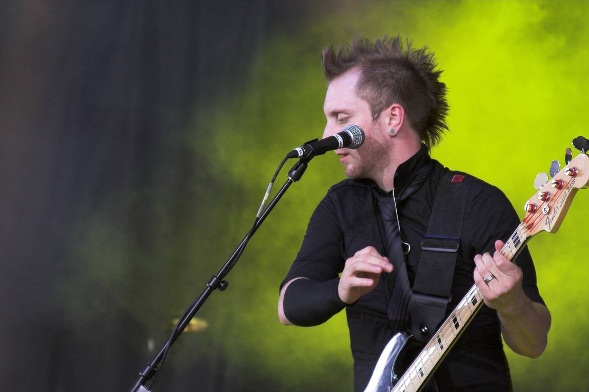 Thousand Foot Krutch bassist Joel Bruyere playing in front of a green lit backdrop