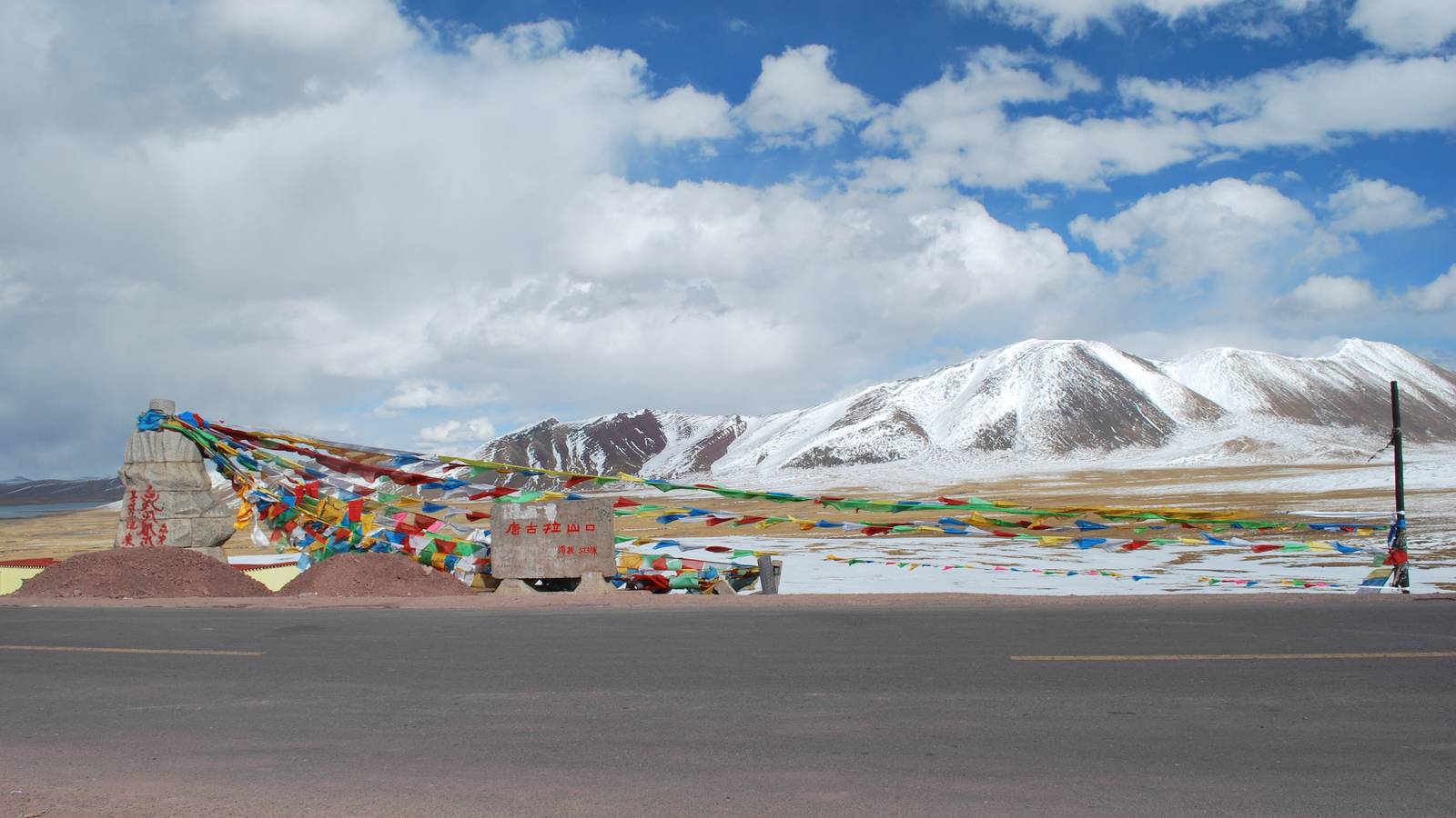 Prayer flags strung beside a road at a high pass in Nagqu, Tibet, with snow covered mountains behind