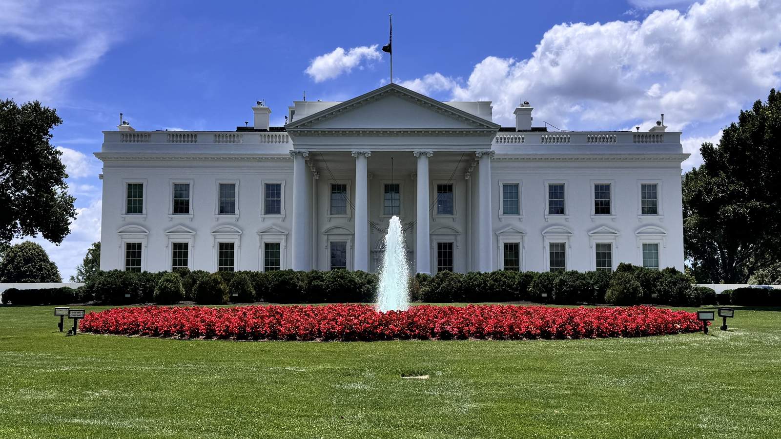 The north facade of the White House seen across the North Lawn with its fountain and a bed of red flowers