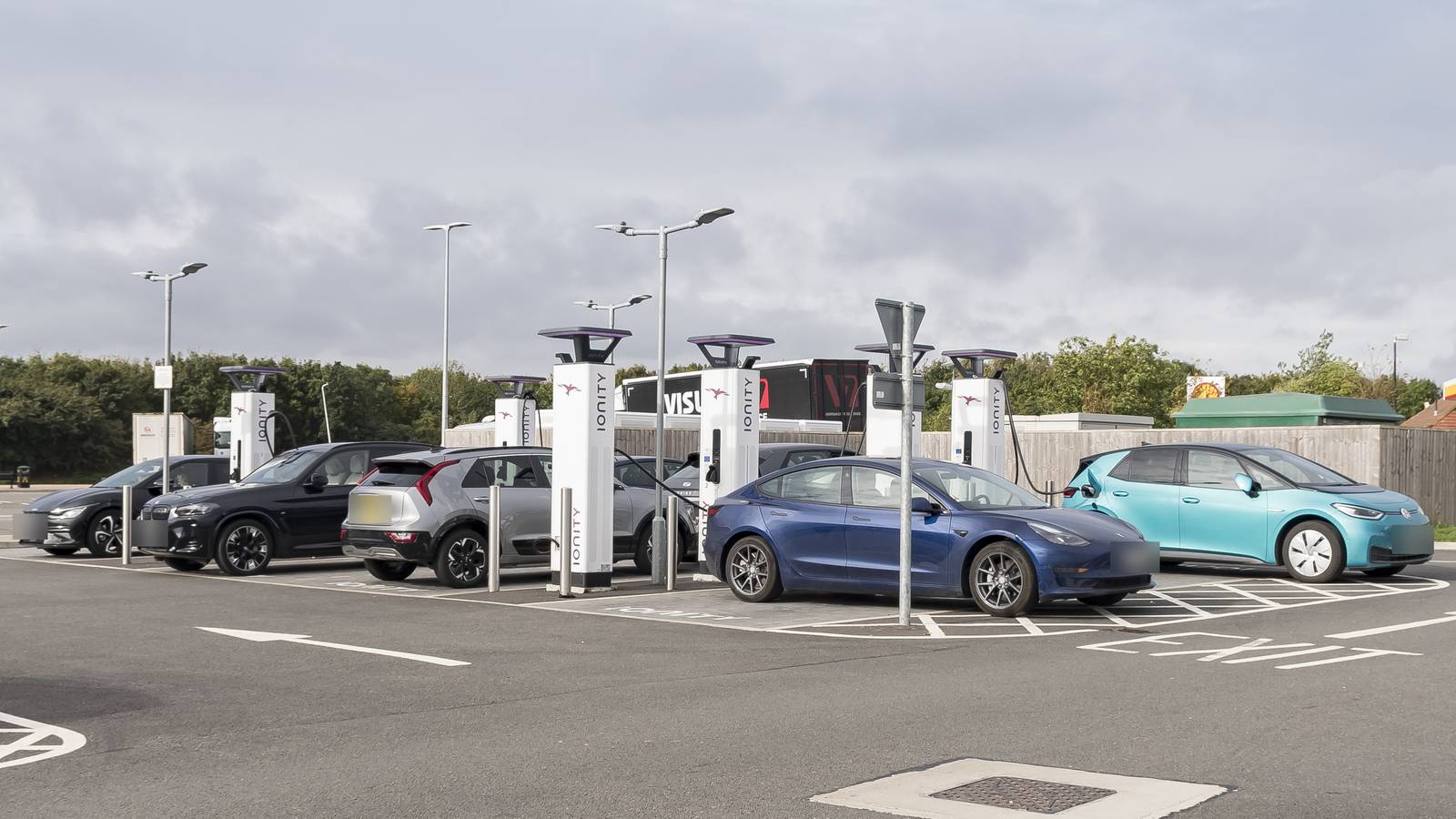 Electric cars plugged in at a row of rapid chargers at a motorway services car park in Cambridgeshire, England