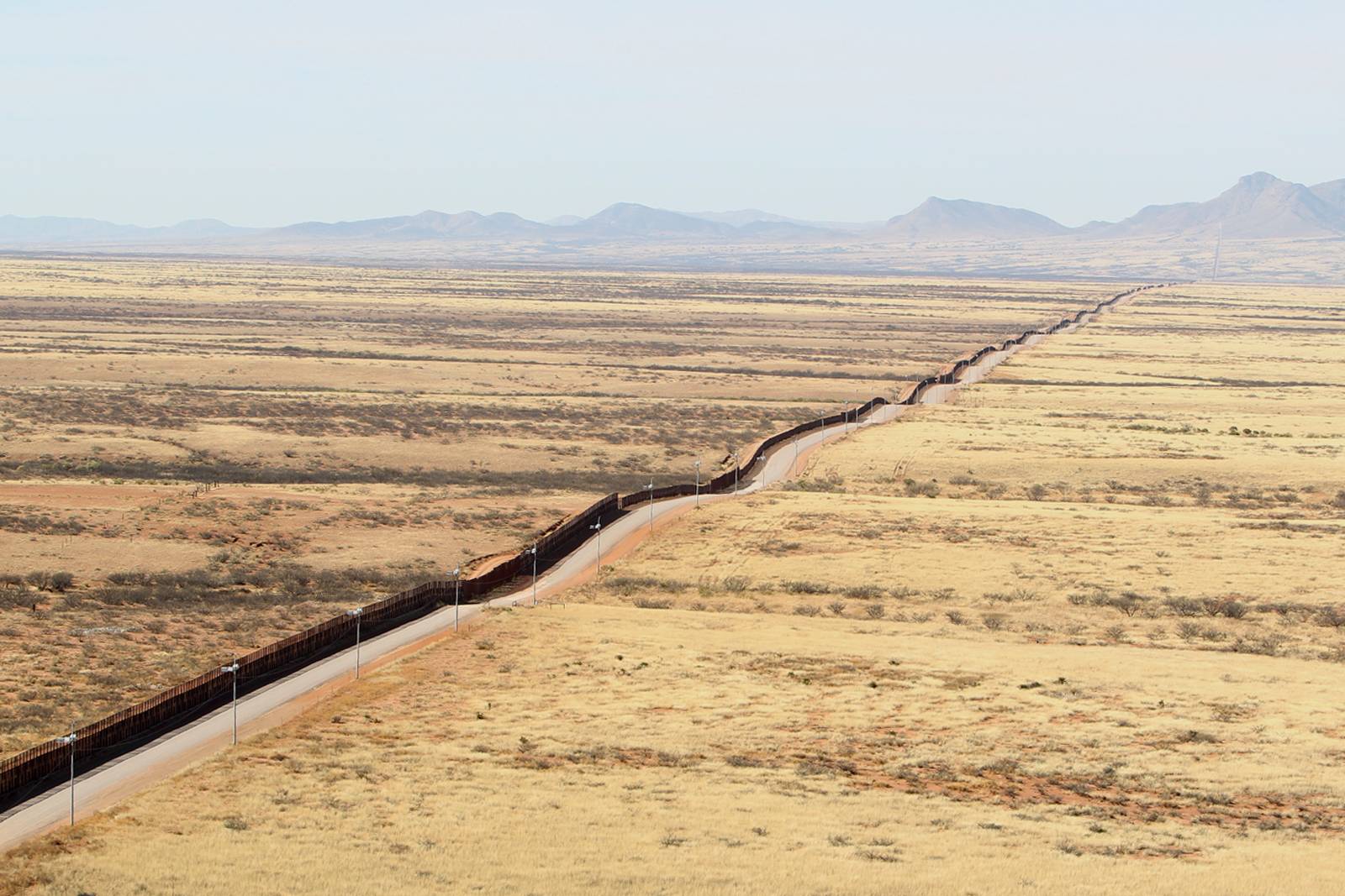 A border fence running across dry grassland towards mountains in Arizona