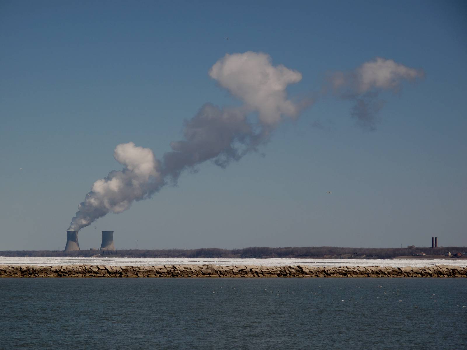 Steam rises from the Perry nuclear plant's cooling towers, seen across Lake Erie past a stone breakwall