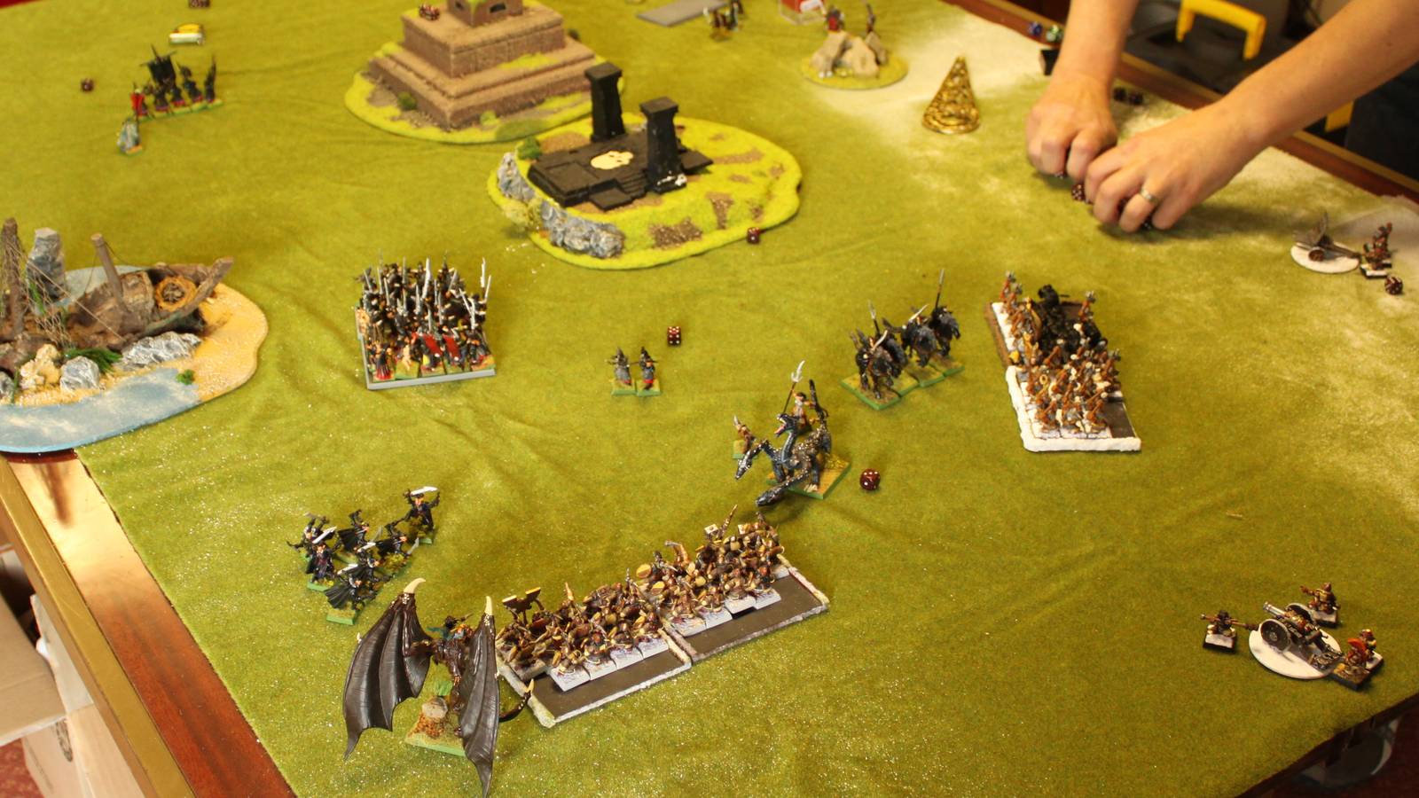 Painted Warhammer Fantasy armies of Dark Elves and Dwarves face off across a green tabletop as a player moves a unit