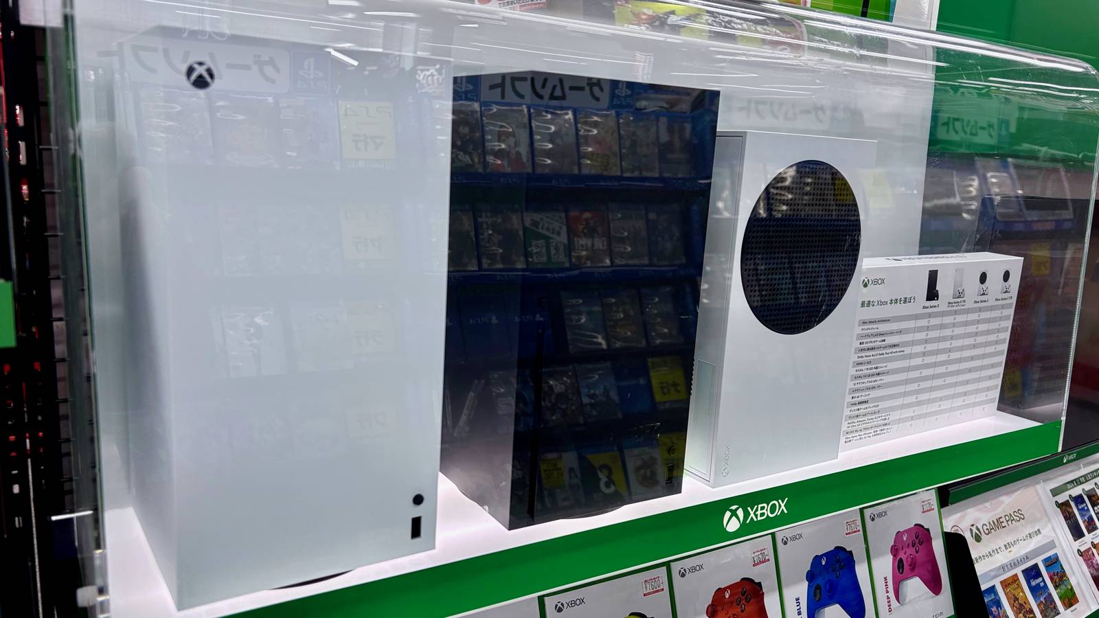 Xbox Series X and Series S consoles in a store display case above a row of boxed controllers