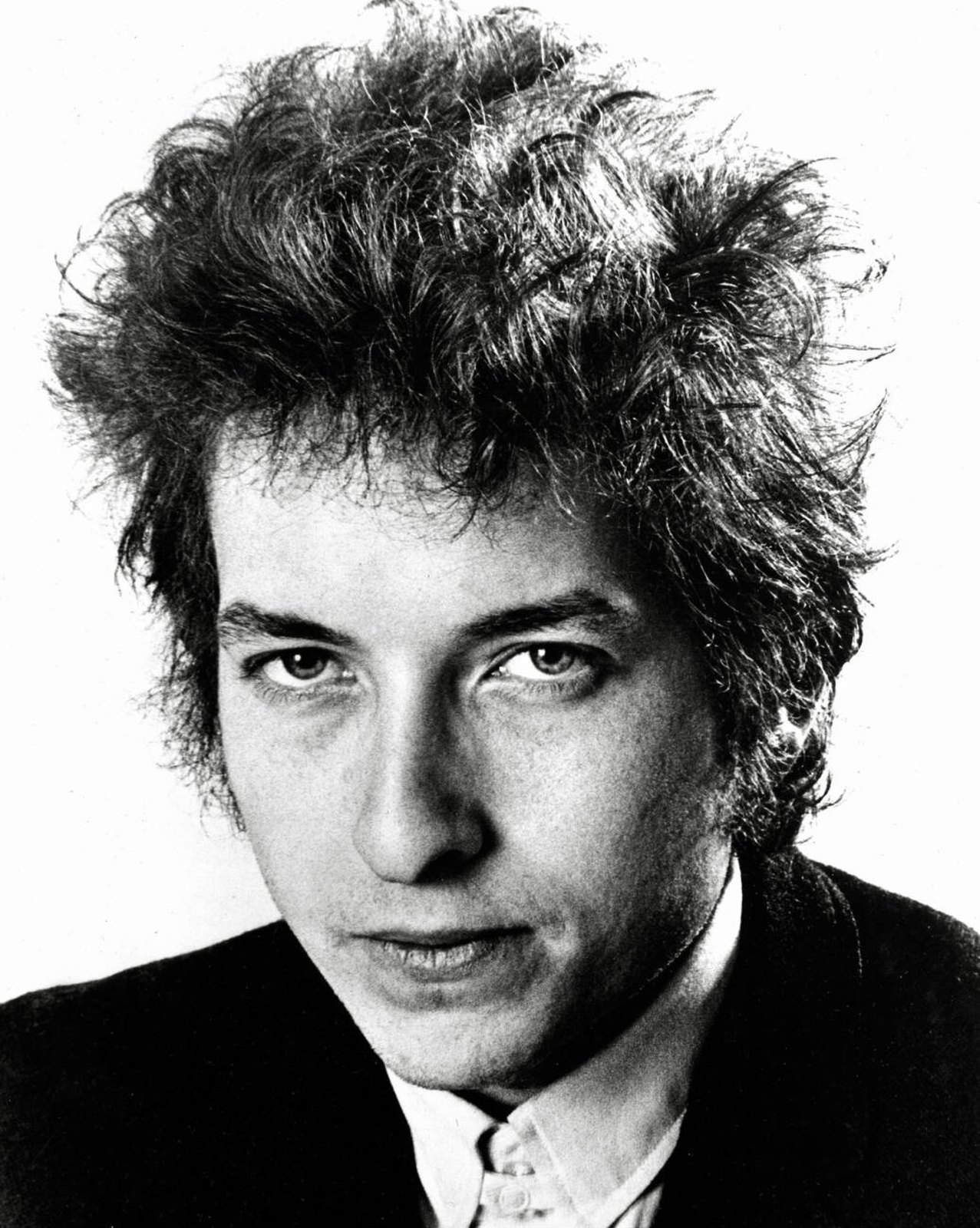 Black and white portrait of a young Bob Dylan with curly hair in a 1965 publicity photo