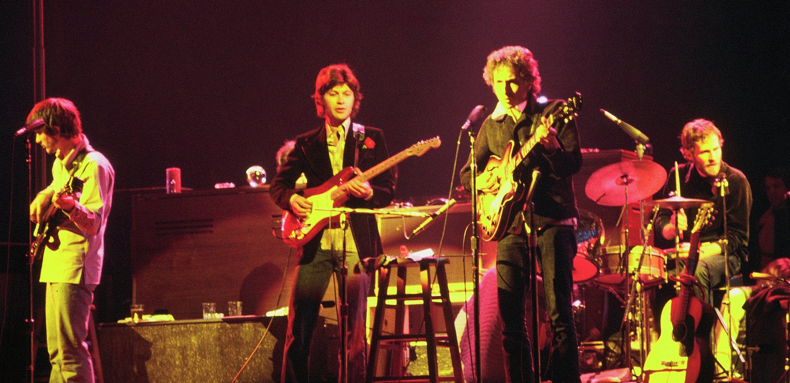Bob Dylan and the Band playing guitars and drums on a red-lit stage in Chicago in 1974