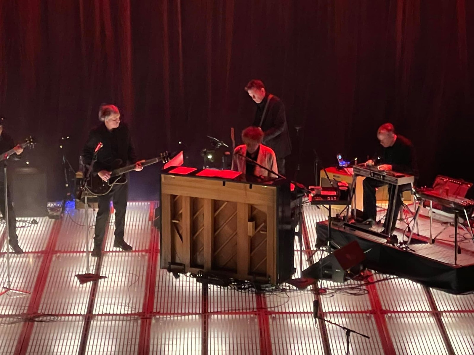 Bob Dylan and his band on a red-lit stage in Milwaukee on the Rough and Rowdy Ways tour in 2021