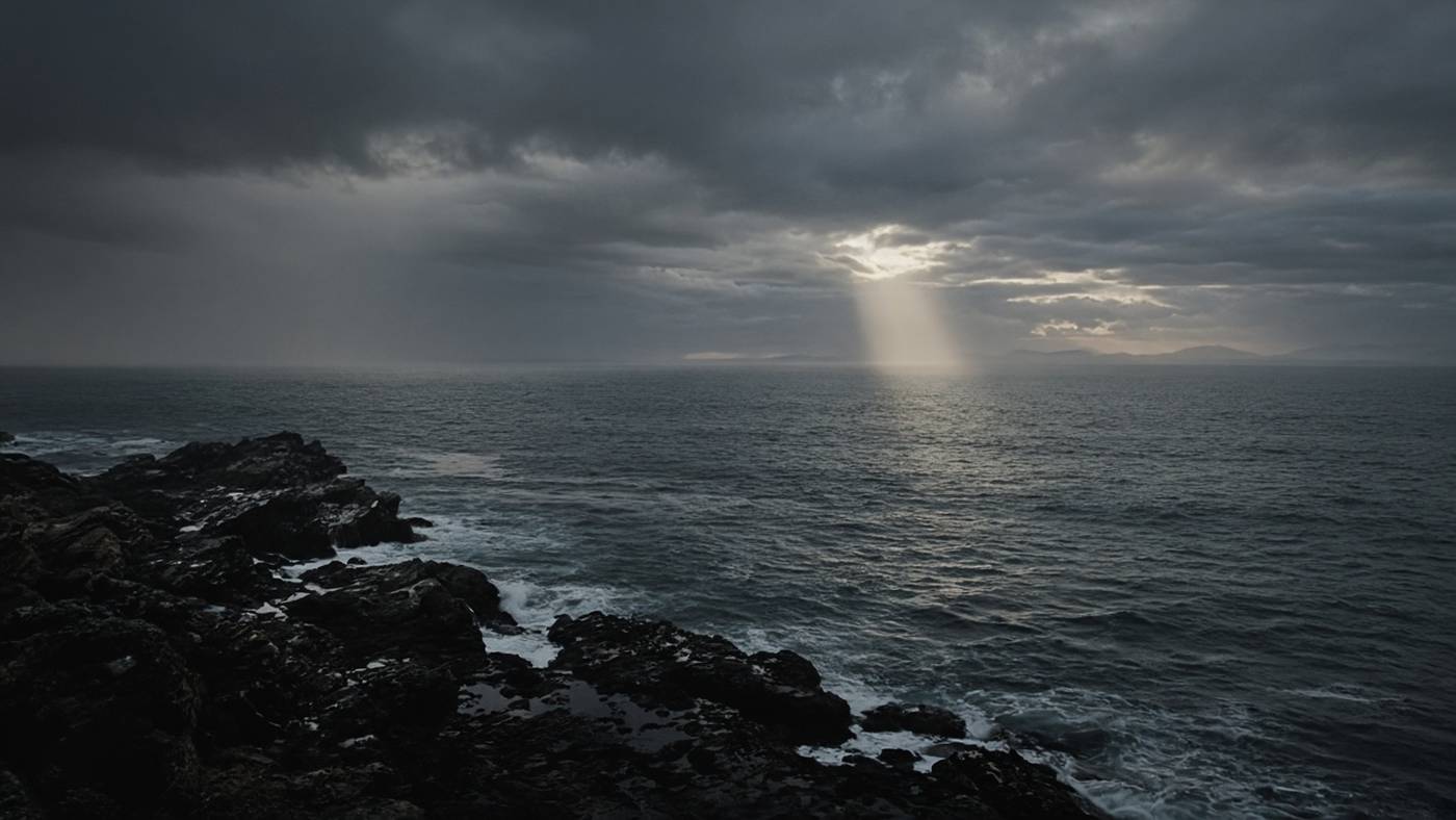 A gray sea under storm clouds with one shaft of light breaking through.