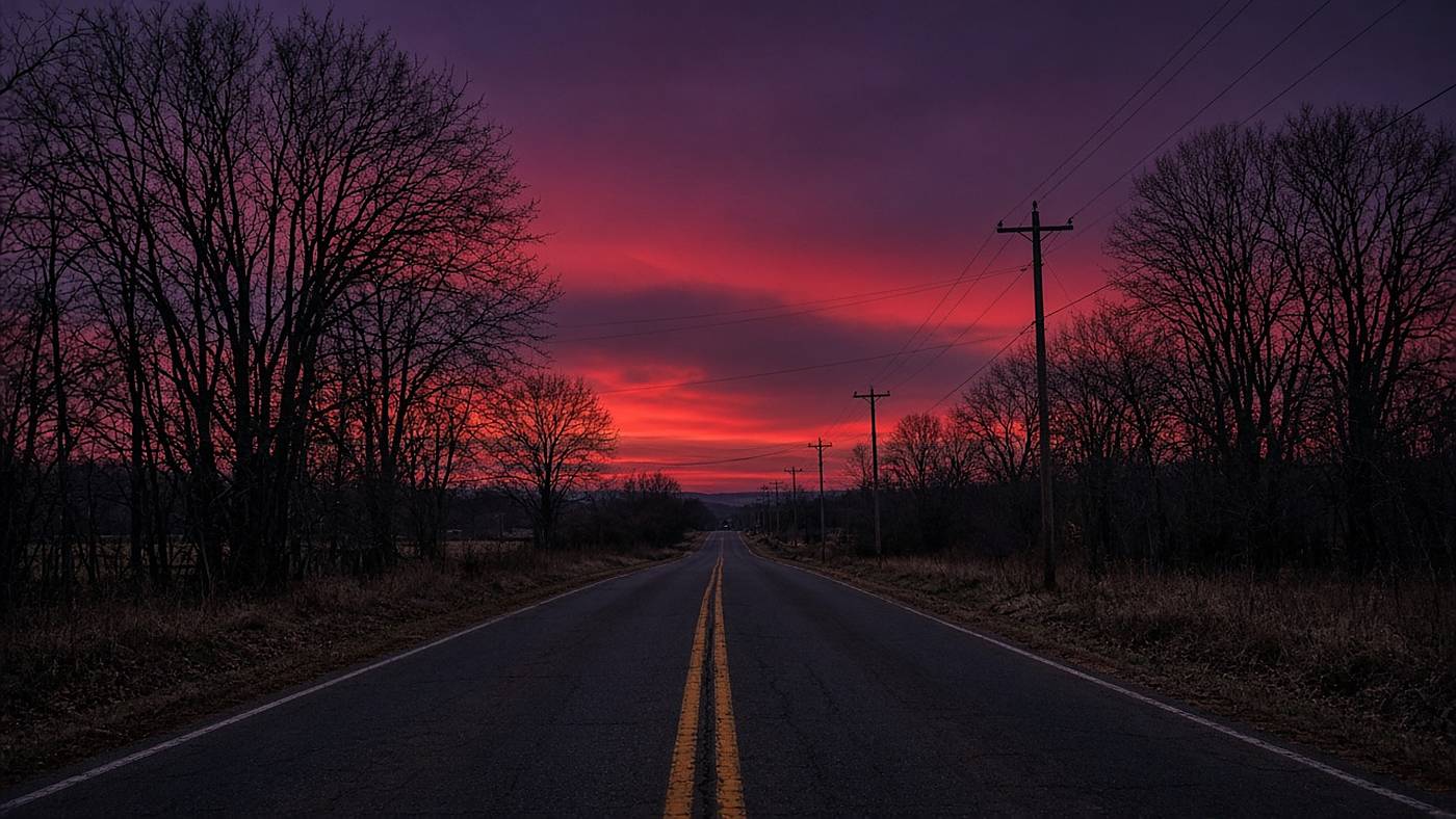 A bare-tree Arkansas back road under a red winter dusk.