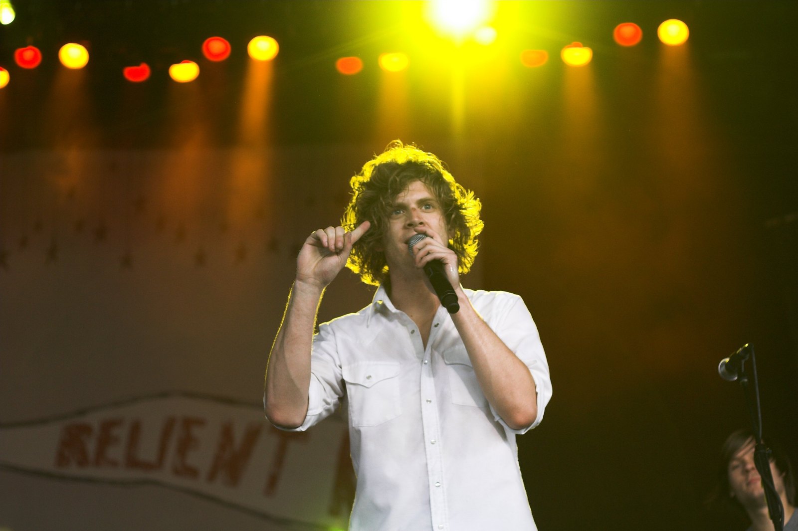 Matt Thiessen singing into a handheld microphone in front of a Relient K banner in 2009