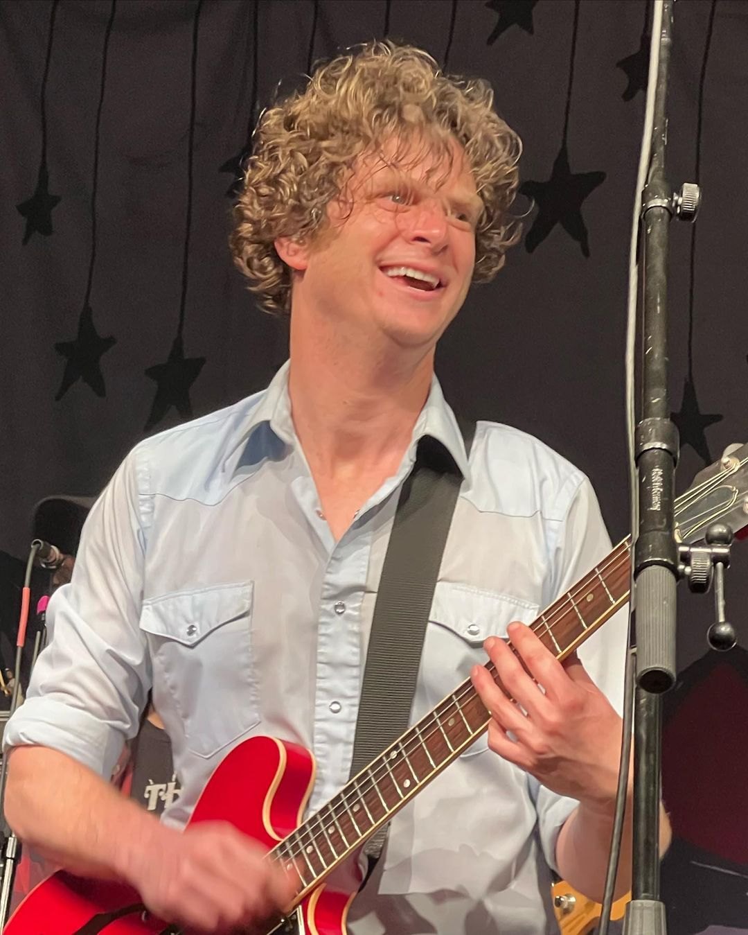 Matt Thiessen of Relient K smiling and playing a red guitar on stage in 2022